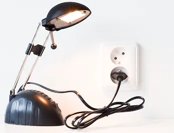 Stolní lampička zapojená do elektrické zásuvky pomocí napájecího kabelu.